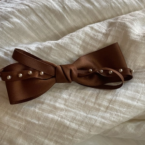 Détail d'une barrette à nœud marron ornée de perles sur un tissu texturé blanc