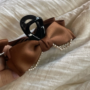 Détail d'une barrette à nœud en satin marron avec perles double rangée et base noire