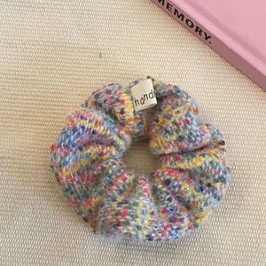 Colorful knitted fuzzy scrunchie with pastel fibers and handmade label on soft fabric