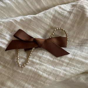 Détail d'une pince à cheveux à nœud en satin marron avec double chaîne de perles
