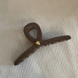 Brown matte shark hair claw clip with golden metal rivet on woven fabric background