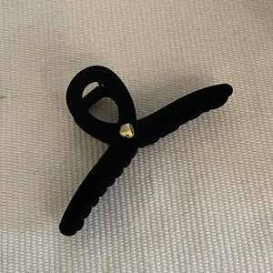 Close-up of black flocked hair claw clip with golden bead detail on woven fabric