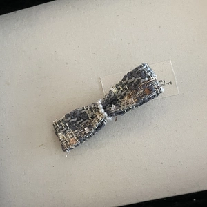 Detail view of tweed bow hair claw with elegant white pearls and metallic gold threading