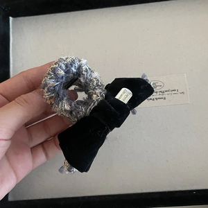 Detail of tweed hair tie with black velvet bow and silver brand-engraved metal tag