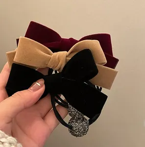 Close-up of velvet bow scrunchies in burgundy, khaki, and black with a crystal ball charm