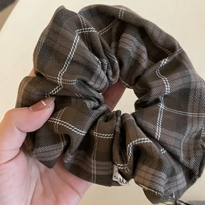 Detailed close-up of brown plaid scrunchie with white stitching and woven brand tag