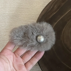 Elegant grey plush hair clip with silver bead accent shown in a hand-held lifestyle shot