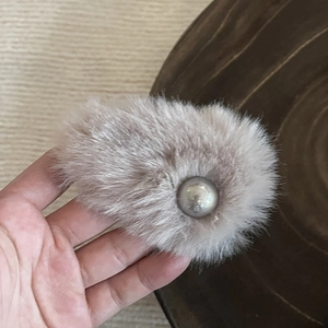 Detail showing hand holding a soft light brown plush faux fur hair clip with a large pearl