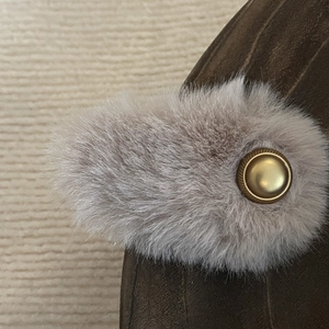 Close-up of plush faux fur trim and golden circular buckle on brown suede hair clip