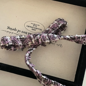Detail of purple tweed bow hair claw clip with golden threads and elegant woven texture