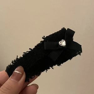 Détail d'une pince à cheveux en tissu noir avec nœud et strass en forme de cœur