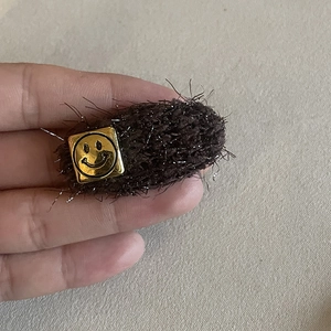 Barrette en peluche marron avec emblème smiley doré tenue à la main