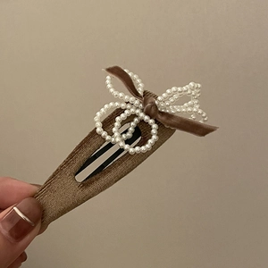 Elegant brown velvet hair clip with pearl bow decoration held by a hand