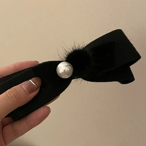 Détail d'une pince à cheveux à nœud noir avec perle factice et pompon en fourrure