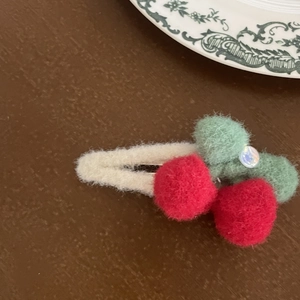 Detail of a handmade red cherry felt hair clip with green leaf on a wooden table