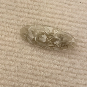 Detailed macro view of an oval acetate hair clip featuring a grey marble pattern with engraving