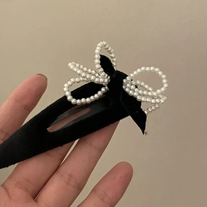 Elegant black velvet BB hair clip featuring a white faux pearl bow on a beige background