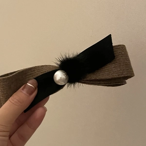 Détail de la pince à cheveux avec nœud en tissu rayé marron, pompon noir et perle