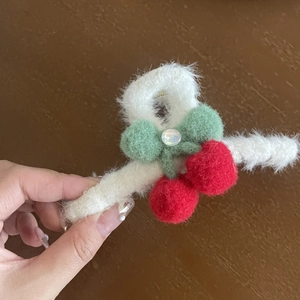 Detail of plush white hair claw clip with red cherry pom-poms and green ribbon bow