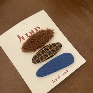 Detailed view of three plush checkered and corduroy hair clips on a white display card