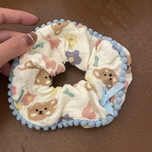 Cute beige scrunchie with bear floral print, blue pom-pom trim and a small ribbon bow