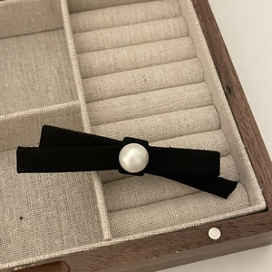 Elegant black suede bow hair clip with white pearl detail in a rustic wooden display box