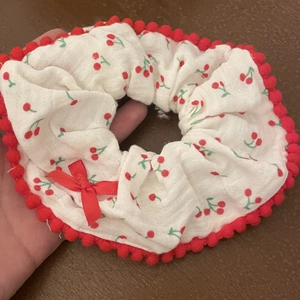 Cute cherry print scrunchie with red pompom edge and bow detail on a wooden desk