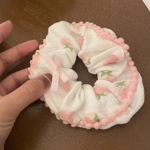 Close-up of strawberry print hair scrunchie with pink pom-pom trim and ribbon bow