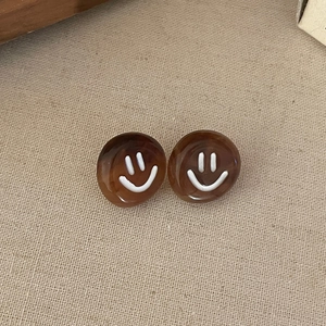 Close-up of amber resin stud earrings featuring minimalist white smiley face designs