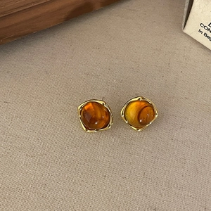 Close-up of vintage amber resin earrings with golden square frames on linen fabric