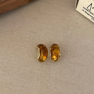 Macro view of amber resin earrings with golden metal edging on a beige linen background