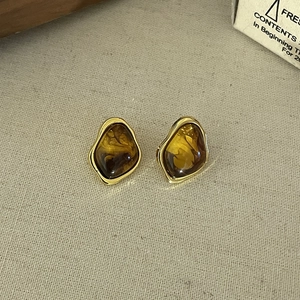 Close-up of vintage amber earrings with irregular gold metal frame on a linen background