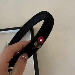 Detail of black velvet padded headband with red embroidered flower and pearl accent