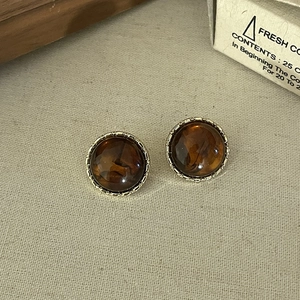 Close-up of vintage amber resin stud earrings with golden textured metal edges