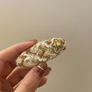 Detail of tweed hair clip with pearl star and gold accents in hand-held view