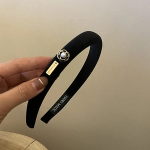 Detailed view of black velvet headband with gold floral charm and white pearl accent