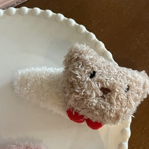 Pinza para el pelo de osito de peluche marrón con lazo rojo en plato decorativo blanco