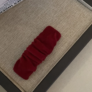 Macro detail of wine red velvet hair clip showing ruched texture on a beige tray