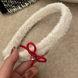 Detail eines weichen weißen Plüschstirnbands mit roter Schleife und funkelndem Kristall