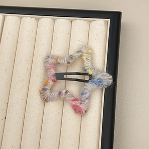 Handmade colorful knit star hair clip with vibrant yarn patterns on a beige tray