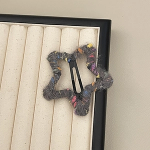 Close-up of star-shaped hair clip with grey knit yarn and colorful speckled textures