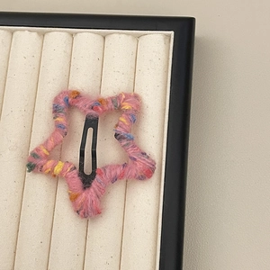 Close-up of pink knitted star hair clip with colorful speckles on a jewelry display tray