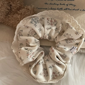 Detailed texture of floral scrunchie with French lace trim and small fabric brand tag