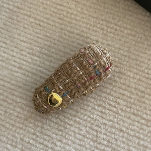 Detailed close-up of a tweed bow hair clip with colorful threads and gold bean accent