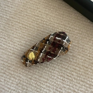 Detailed close-up of a tweed bow hair clip with gold geometric metal buckle accent