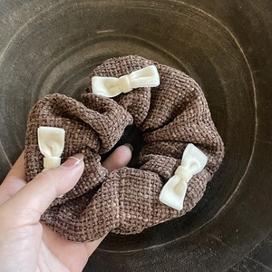 Detailed close-up of a brown woven scrunchie with three white velvet mini bows