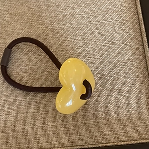 Detail of yellow heart resin charm on elastic dark brown hair tie with a glossy finish