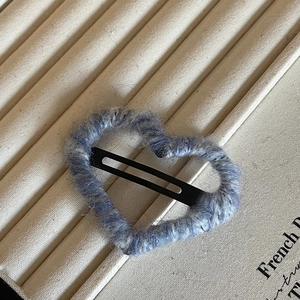 Detail of heart-shaped hair clip wrapped in blue and white wool yarn on a display case