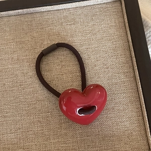 Detailed view of a glossy red heart charm on a high-elastic brown braided hair tie