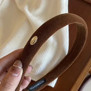 Close-up of brown corduroy headband with a gold logo and a handmade textile label